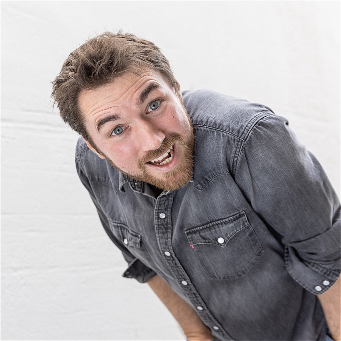 Comedian looking into camera with a mischievous smile.