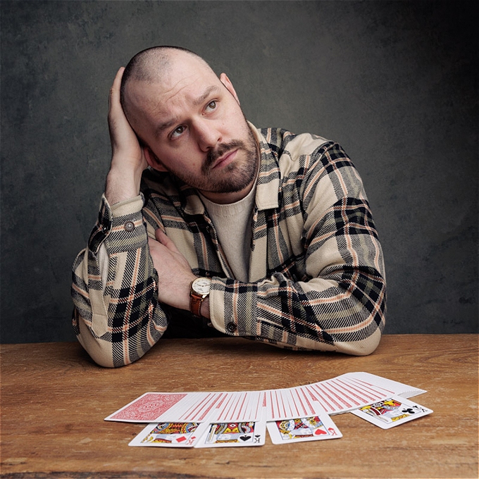 Andrew Frost looks up and away off camera. In front on him is a deck of cards spread out with the 4 kings showing face up amongst the rest of the deck