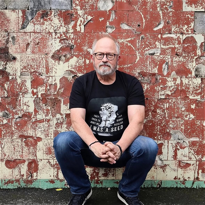 A bespectacled and casually dressed Robin Ince, crouching and looking pensive