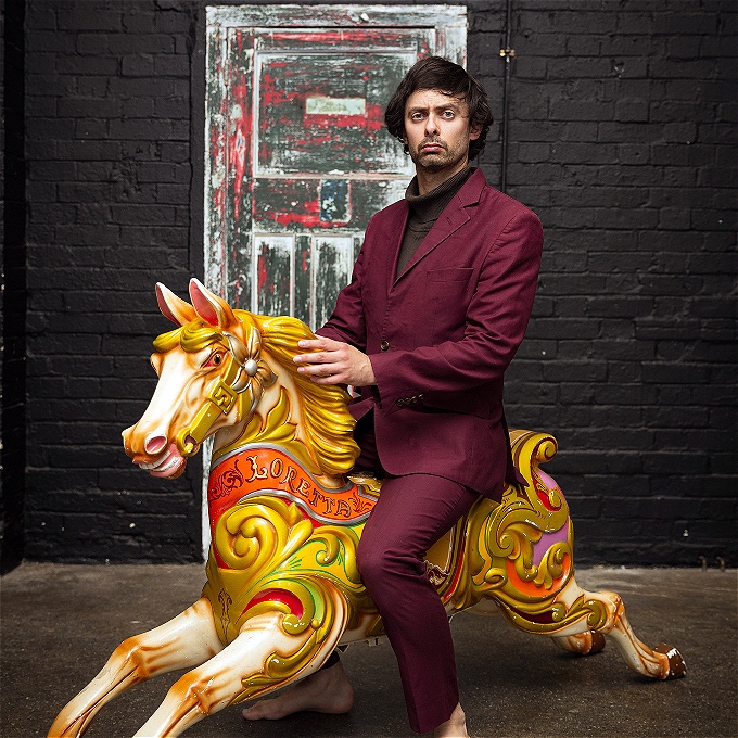 Marcel Lucont in a burgundy suit sitting upon a fairground horse