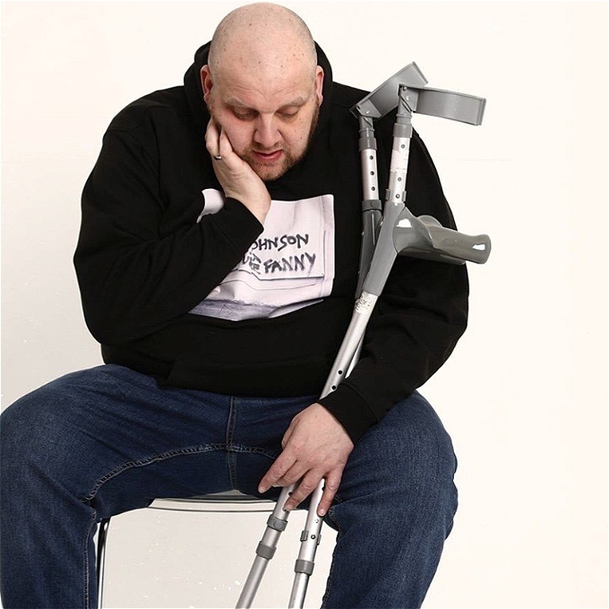 Bald and disabled comedian, sits holding his crutches, and questioning how life became what it is
