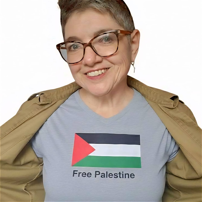 Female comedian Daphna Baram wearing glasses and smiling with black background and black clothes