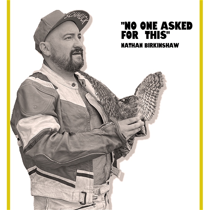 A black and white image of a comedian in motorcycle leathers holding a kestrel.
