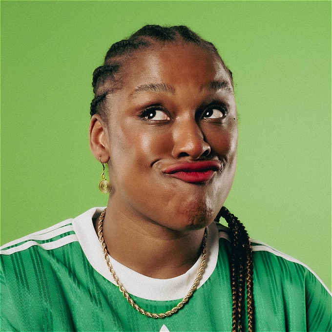Black female comedian, makes funny face using her lips wearing a green Adidas shirt.