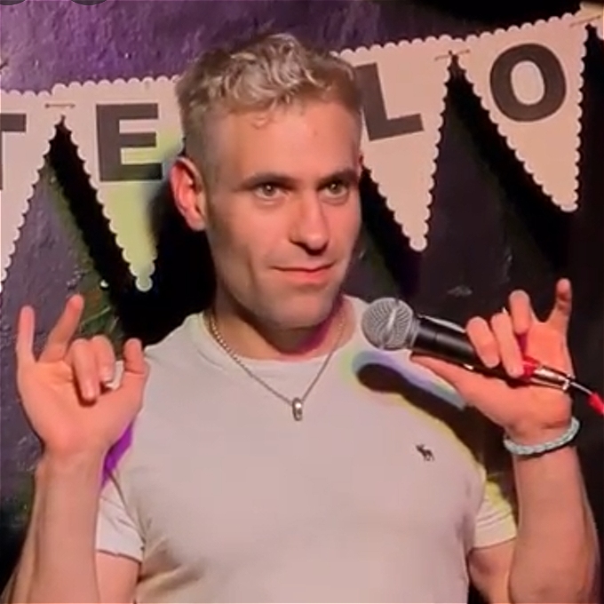 Male comedian in a hands up pose holding a microophone as part of a story